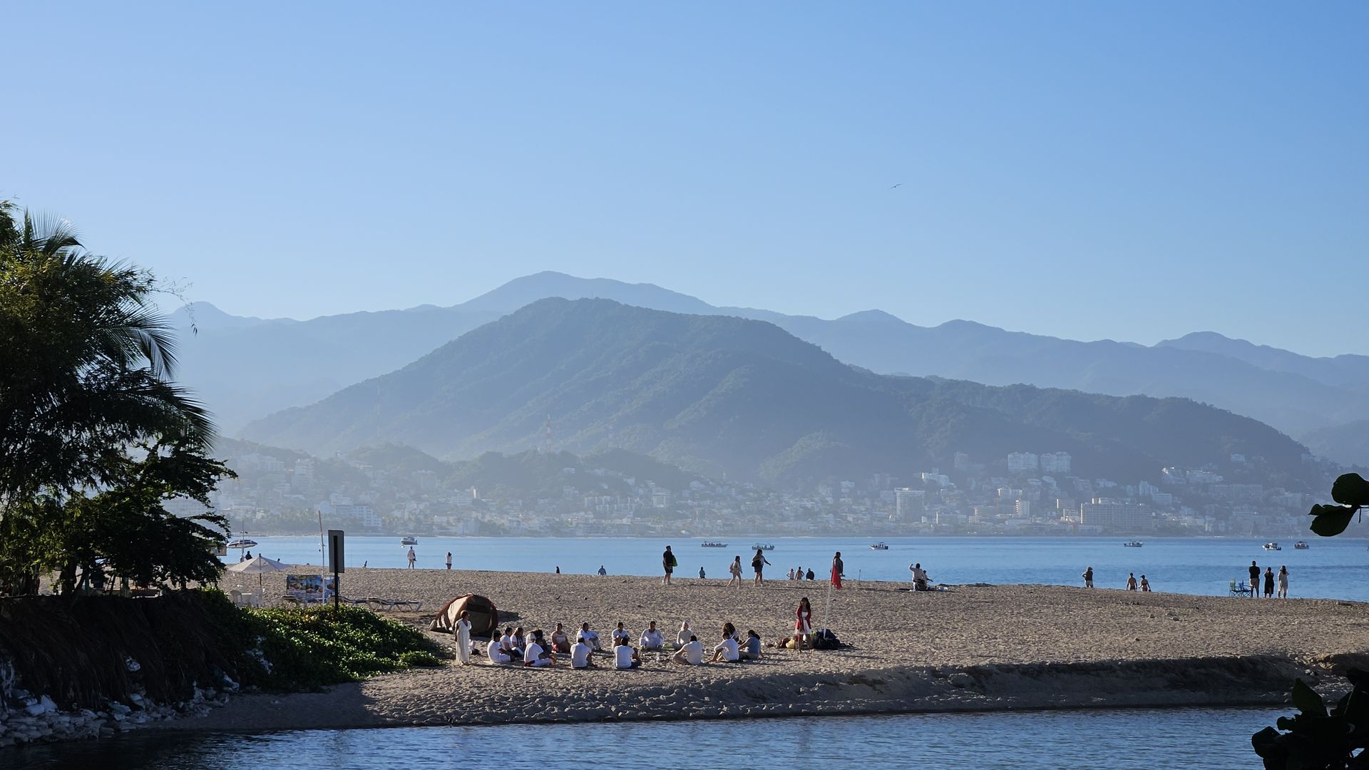 A group wellness practice on the beach with the mountains of Puerto Vallarta beyond